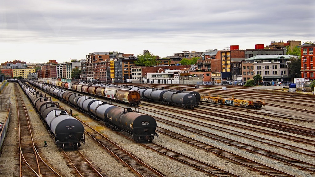 Train yard with trains, rail tracks, and background buildings. 