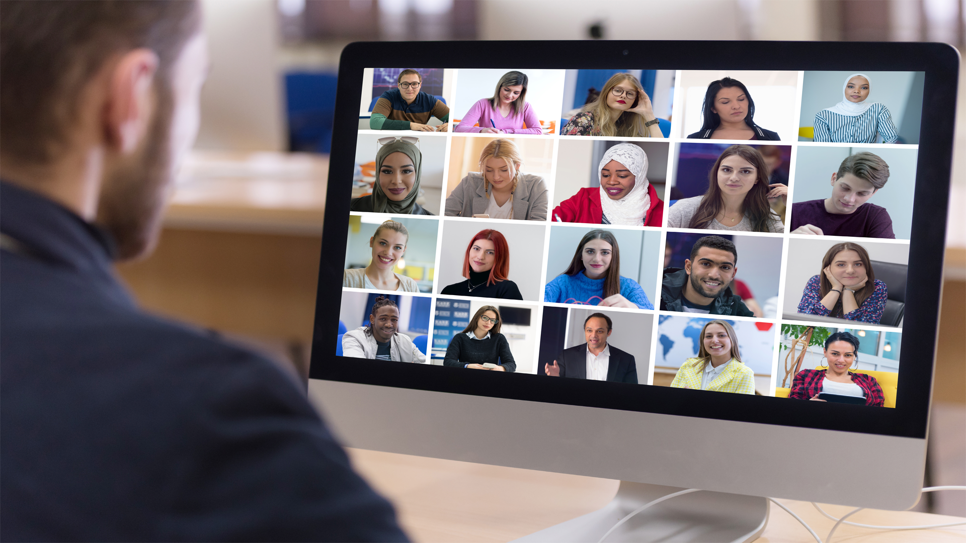 Man by computer with 20 tiles of different people on the screen