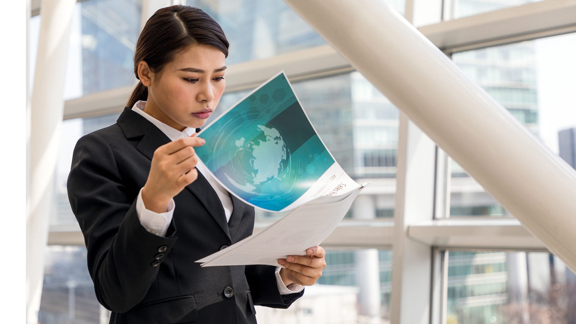 Women reading a report in the office building next to a large window.