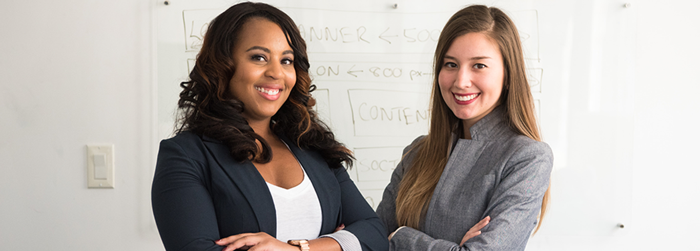 two ladies standing with arms crossed smiling 