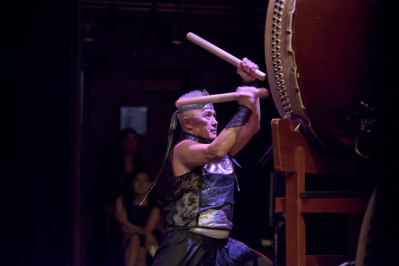 Man on stage striking a hug horizontal drum