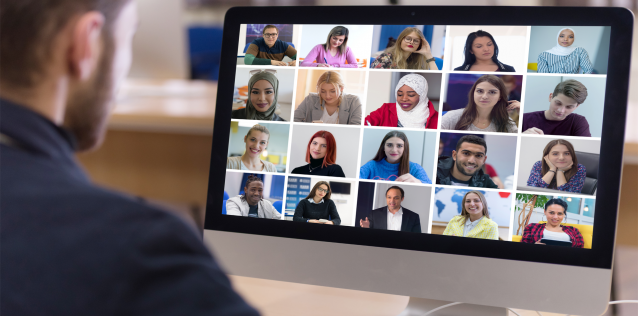 Man by computer with 20 tiles of different people on the screen